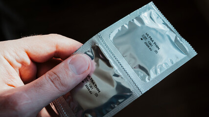 Silver packaging condom, two ultra thin condoms in hand, black background. Concept of contraception...