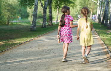 Fototapeta na wymiar A photo from the back of two little girls sisters walking together on a path in the park. The concept of children's love and friendship, best friends forever. High quality photo