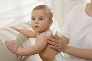 Mother applying body cream on her little baby at home, closeup