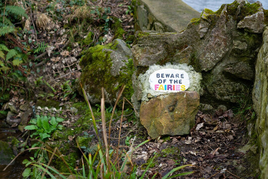 Hand painted Beware of the Fairies sign on stone rock wall in fairy garden in woods.