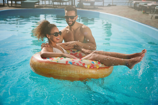 Happy couple with inflatable ring in outdoor swimming pool on sunny summer day