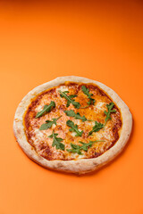 Pizza Margherita with mozzarella, pilati sauce with cherry tomatoes, arugula, oregano and basil. Orange background. copy space