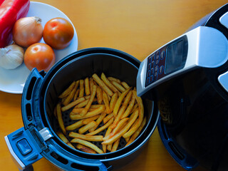 Top view of an air fryer on a table with french fries and vegetables.