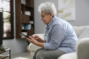 Elderly woman with poor posture using tablet in living room - obrazy, fototapety, plakaty
