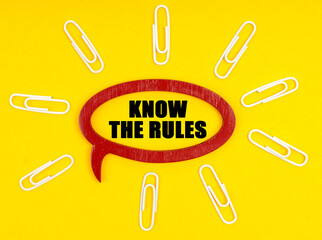 On the yellow surface are paper clips, and a plate inside which the inscription - KNOW THE RULES