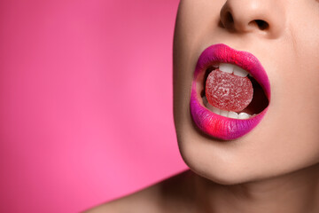Young woman with beautiful makeup holding candy in lips on pink background, closeup. Space for text