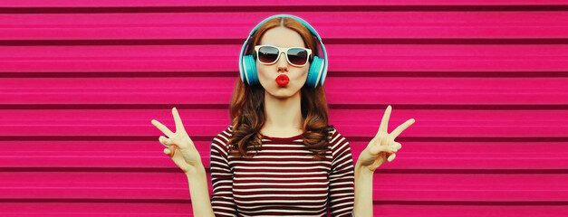 Portrait of cheerful young woman with headphones listening to music on colorful pink background