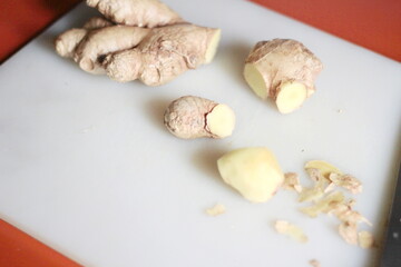 Ginger is being sliced on a plastic chopping board with a knife on an orange table.