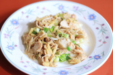 Ginger-fried chicken with sliced spring onions served on a white floral plate on an orange dining table.