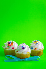 Three vanilla frosting cupcakes with front one wrapped in a bow tie placed on bright green background.