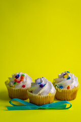 Three white frosting cupcakes on yellowish green background