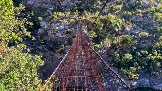 Point of view video. Slowmotion shot of a person walking along old metal rope bridge across the Moraca river canyon in Montenegro