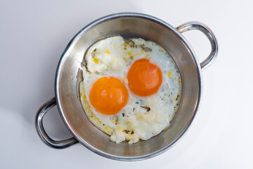 Cropped view of broken fraternal eggs in pan, shot with selective focus from overhead angle on white background in isolated setting.