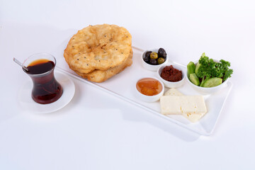 Cropped view of plate of greens, tomato paste, olives, citrus jam, cheese slices, cup of tea and bagels on white plate, shot with selective focus on isolated white background from opposite angle.