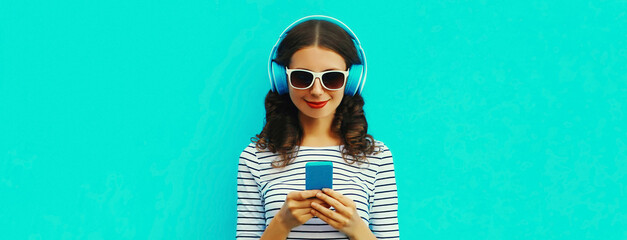 Portrait of smiling young woman in headphones listening to music with smartphone on blue background