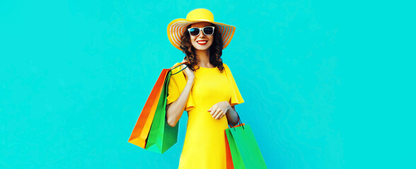 Portrait of beautiful happy smiling young woman with shopping bags wearing summer straw round hat on blue background