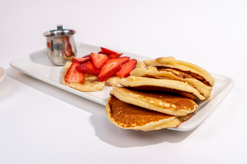 Close-up shot of pancakes, banana and strawberry slices and hot chocolate on white plate shot with selective focus from opposite angle on isolated area, white background.