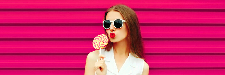 Portrait of stylish young woman blowing her lips sending sweet air kiss with red lipstick wearing...