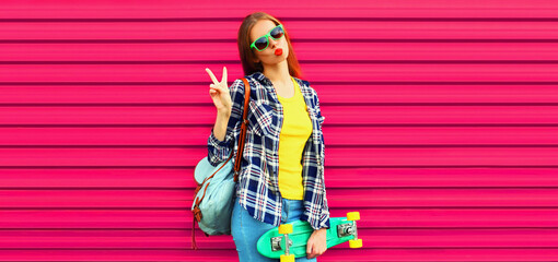Portrait of stylish young woman model with skateboard wearing shirt, sunglasses and backpack on vivid pink background © rohappy