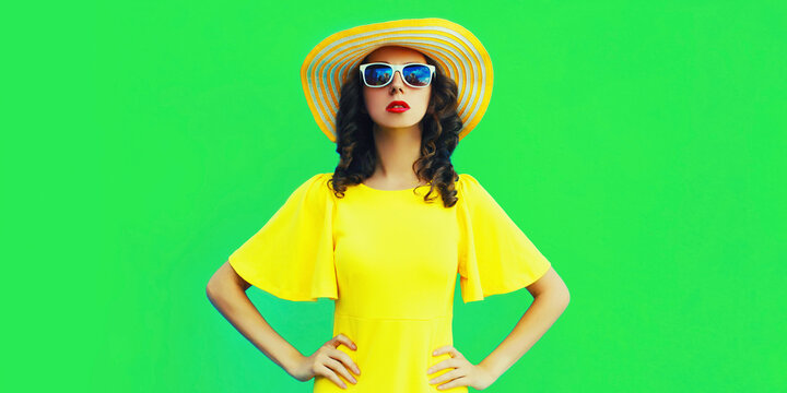 Portrait of beautiful young woman wearing yellow summer hat and dress on green background