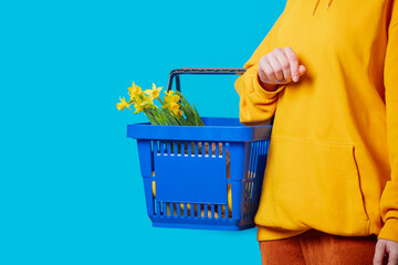 Fototapeta premium Stylish female in yellow hoodie with blue basket and flowers on blue background