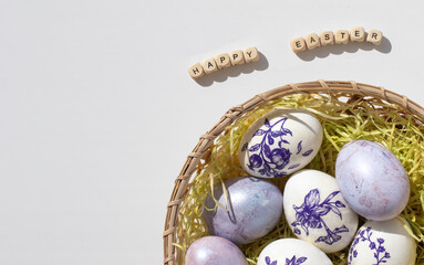 Easter concept. Purple eggs in a wicker basket with straw on a white background. Minimalism.
