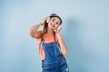 hispanic young woman with headphones, dancing and listening music on blue background in Mexico Latin America