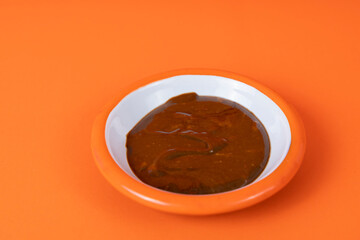 Close-up shot of tahini and molasses mix and white plate with orange rim, shot with selective focus from opposite or side angle on isolated area, orange background.