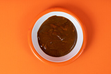 Cropped view of tahini and molasses mix and white plate with orange rim shot with selective focus from top angle on blue background in isolated area.