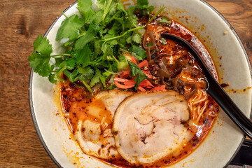 Spicy Shoyu Ramen, Japanese noodle soup, with pork belly Chashu and cilantro, on wooden table.