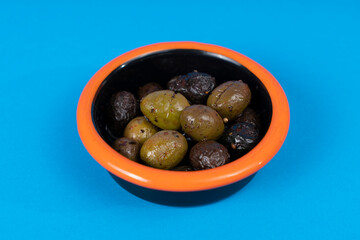 Close-up shot of black plate with orange rimmed black and green olives in isolated area, blue background with selective focus from opposite or side angle.