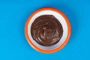 Cropped view of black plate with hazelnut chocolate cream and orange rim, shot with selective focus from overhead angle on blue background in isolated area.