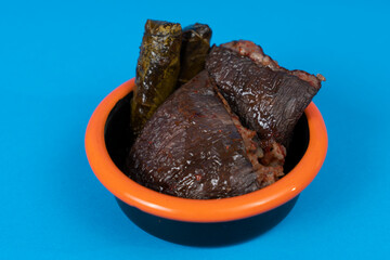 Close-up shot of traditional turkish food stuffed and wrapping black plate with orange rim, shot in isolated area, blue background with selective focus from opposite or side view.