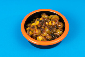 Close-up shot of olive sauce with corn and black plate with orange rim shot with selective focus from opposite or side angle on isolated area, blue background.