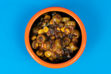 Cropped view of olive sauce with corn and black plate with orange rim shot with selective focus from overhead angle on blue background in isolated area.