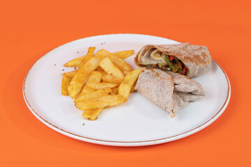 Cropped view of french fries and sliced veggie wrap on isolated orange background shot with selective focus from opposite or side view.