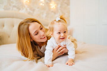 Cute mom and baby daughter lie down, play and hug in bed. games with children. 