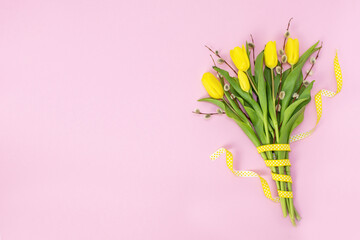 Springtime and Easter holiday pastel pink background. Beautiful spring bouquet of yellow tulips with willow branches and a polka dot ribbon. Copy space for text.