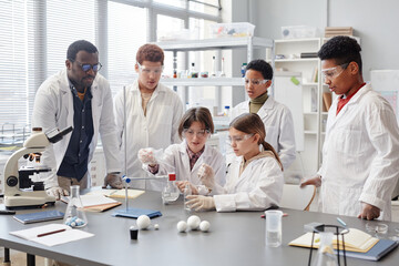 Large group of diverse children wearing lab coats in chemistry class while enjoying science...