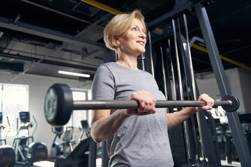 Fototapeta na wymiar Joyful woman doing exercise with barbell in gym