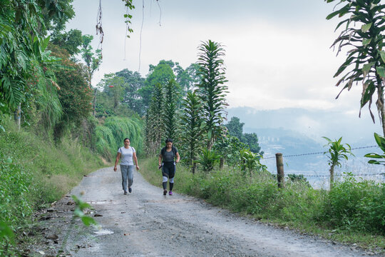 mother and daughter walking along a dirt road (trocha) on top of a Colombian mountain in the coffee region near the city of Pereira-Colombia, surrounded by nature and coffee crops. hiking concept