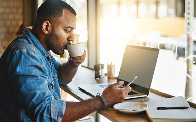 Making full use of the fast wifi at his local cafe. Shot of a handsome young man drinking coffee while working working in a cafe.