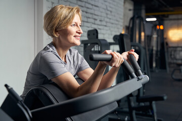 Fototapeta na wymiar Cheerful woman using gym equipment in fitness center