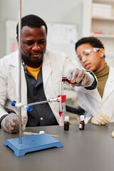 Vertical portrait of African American teacher demonstrating science experiments in school chemistry...