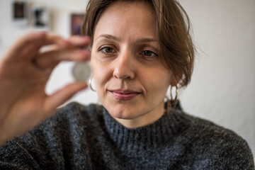 Portrait of Ukrainian Woman Looking at Silver Hryvnia Coin from her Country Thinking How to Save Money