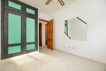 Empty room with light stoneware floor, mirror on the wall and closet with plain green and black painted doors