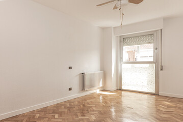 empty room with herringbone oak parquet and freshly painted walls, with a large window and ceiling fan