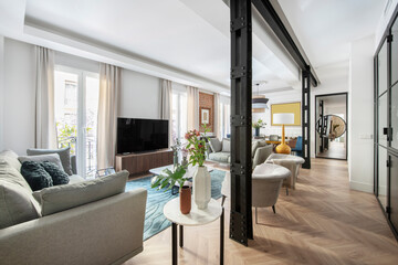 Living room with beautiful contemporary decor with gray fabric sofas, armchairs, vases with plants and flowers and exposed black painted steel beams and columns