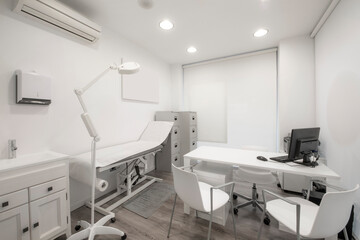 Paper-topped table in a beauty clinic with gray file cabinets, a desk with a computer and white chairs with a magnifying lamp