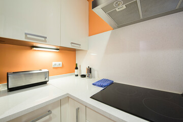 Corner of a kitchen with a white stone countertop and orange walls with a ceramic hob, a coffee maker and a toaster on the counter